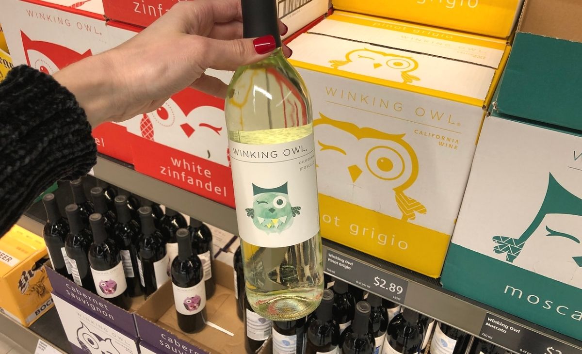 A hand grabbing a bottle of wine off of a shelf at the store cheap liquor