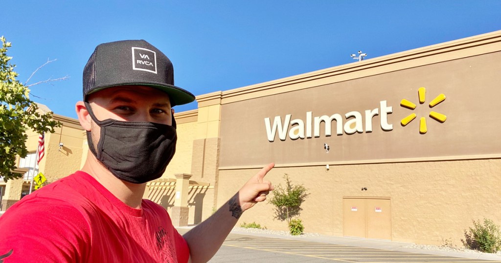 man in red shirt and black hat pointing at walmart sign while wearing black face mask