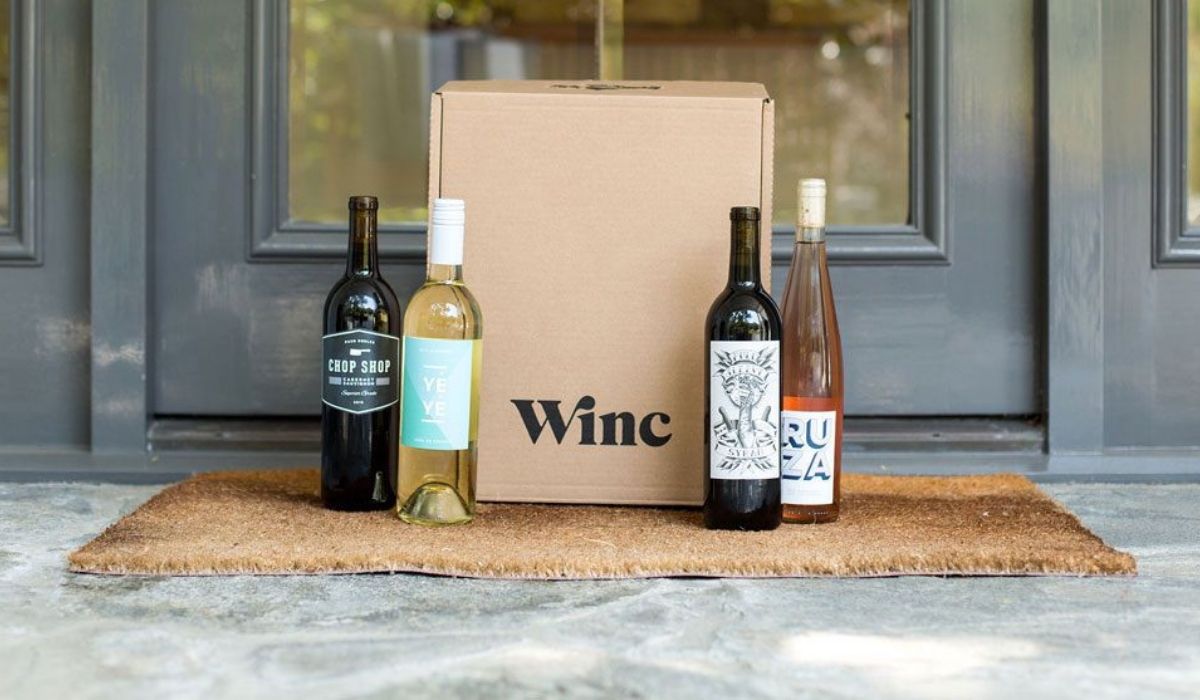A wine subscription box on a porch next to wine bottles