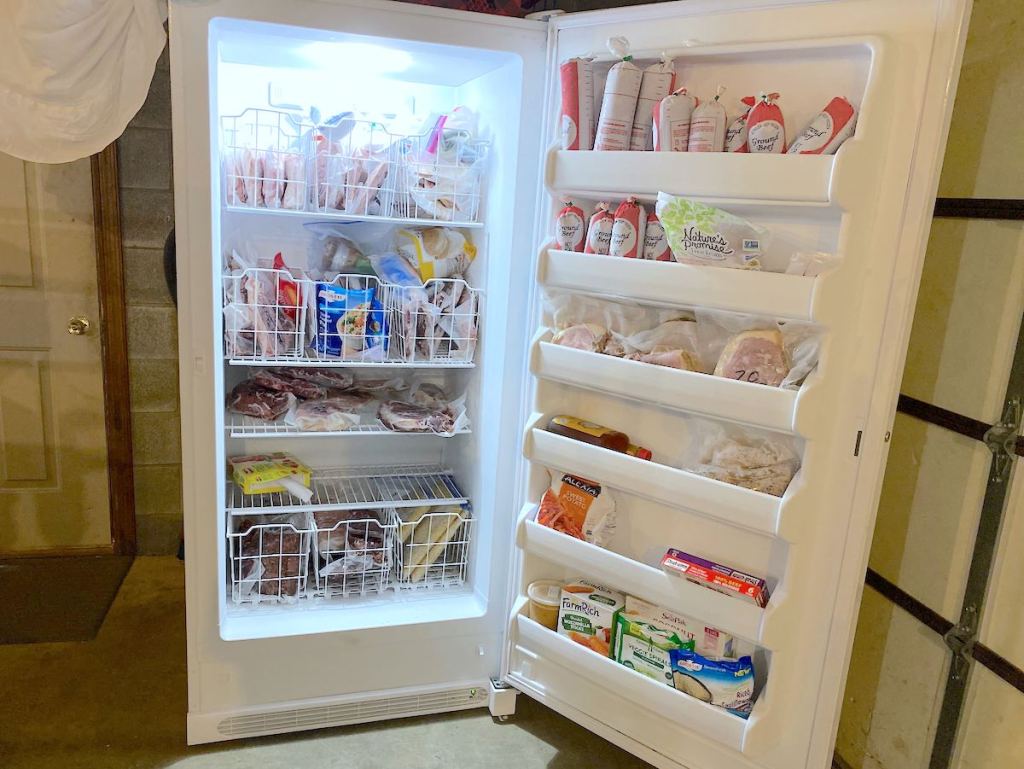 white stand up freezer in garage with various types of meat and food