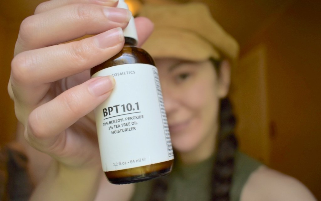 woman holding bottle of benzoyl peroxide beauty products