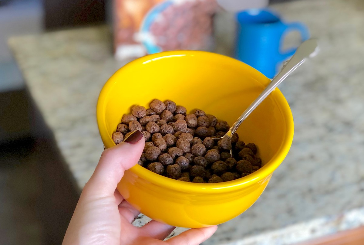 hand holding a yellow bowl with chocolate cocoa puffs inside