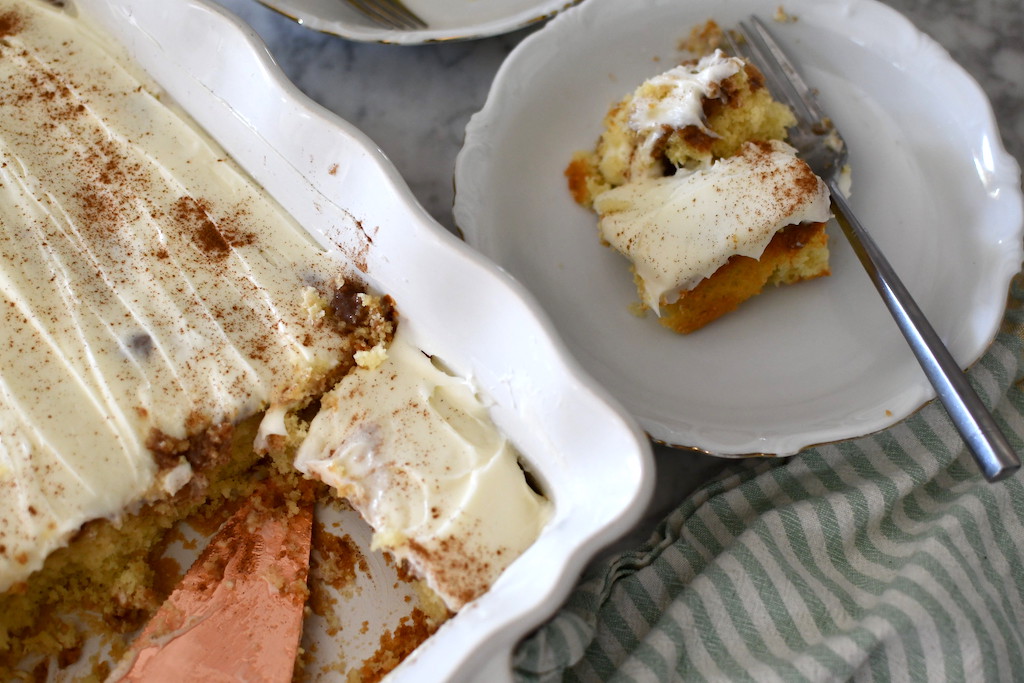 cinnamon roll poke cake in casserole dish with slice on plate