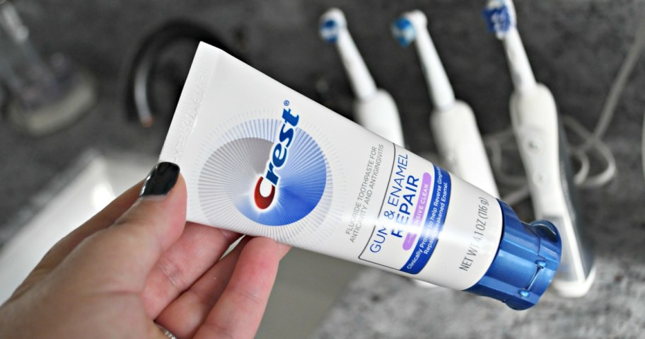 hand holding up crest toothpaste over sink 