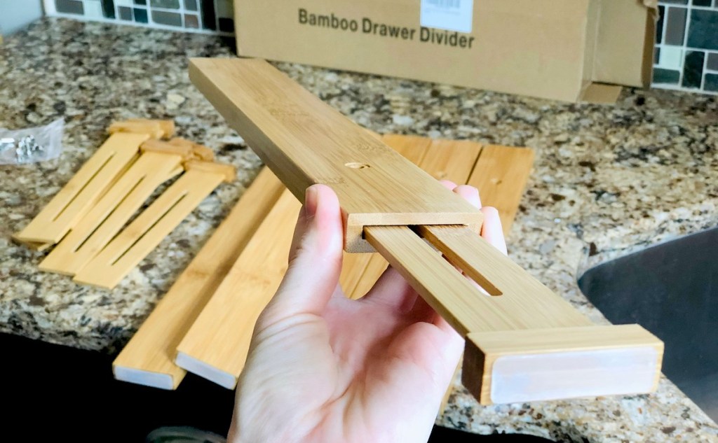 hand holding a bamboo drawer divider with box and other dividers on counter