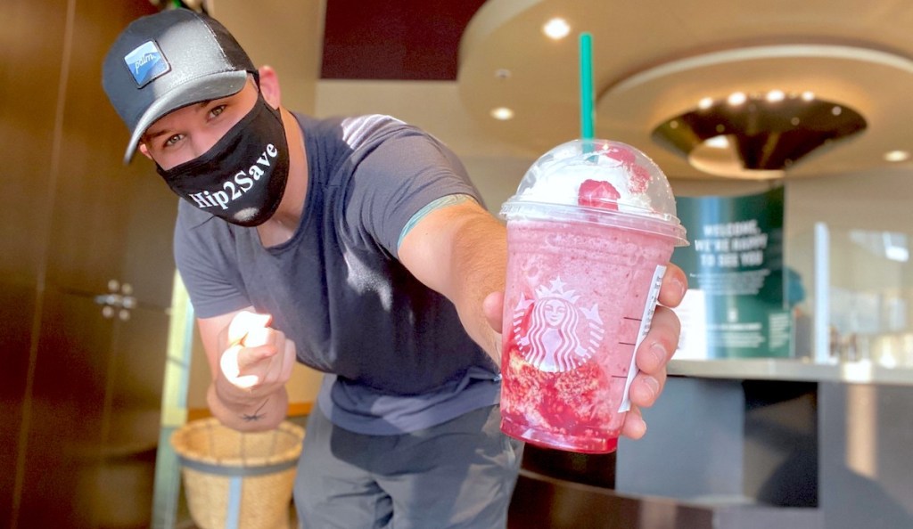 man holding and pointing to a pink starbucks drink with straw and whipped cream