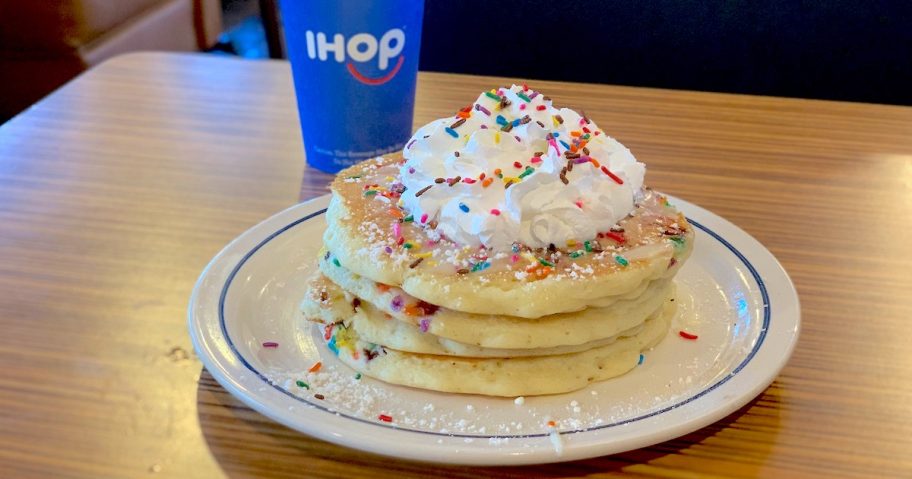 stack of pancakes with whipped cream and sprinkles with blue ihop cup behind plate