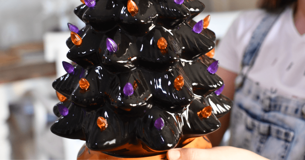 person holding a black tree with orange and purple lights on it