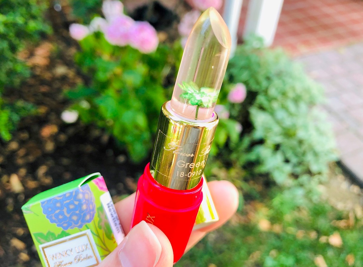 hand holding hot pink and gold lipstick with green flower inside