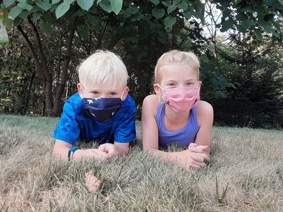 two kids lying on grass wearing face masks