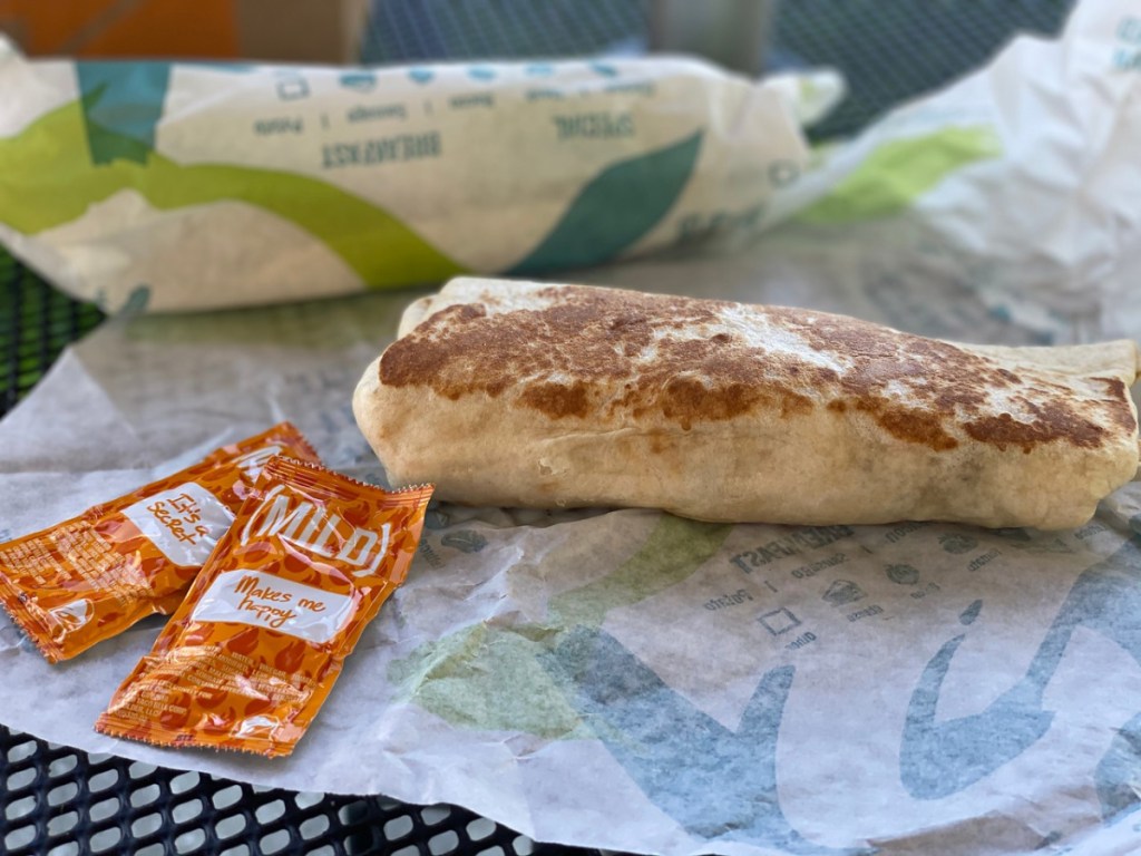 burrito sitting on table by packets of hot sauce
