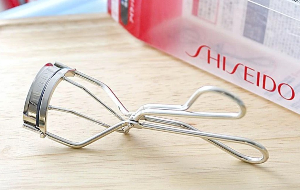 silver eyelash curler sitting on light wood table with box