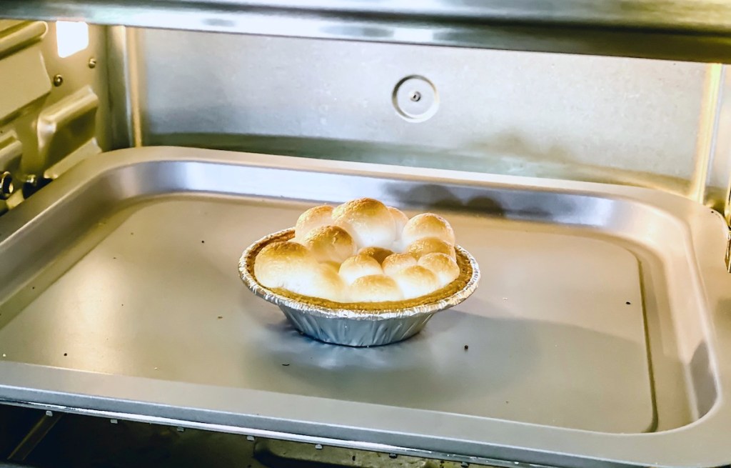 mini pie crust with roasted marshmallows on top sitting on stainless steel tray in oven