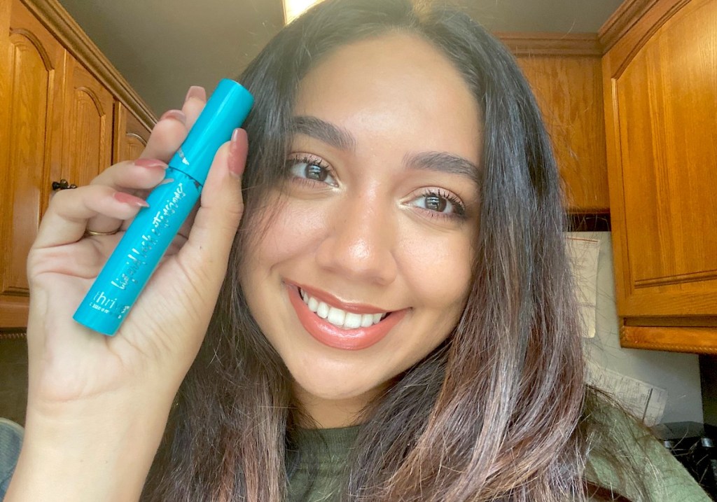 woman smiling holding blue tube of thrive causemetics mascara beauty products