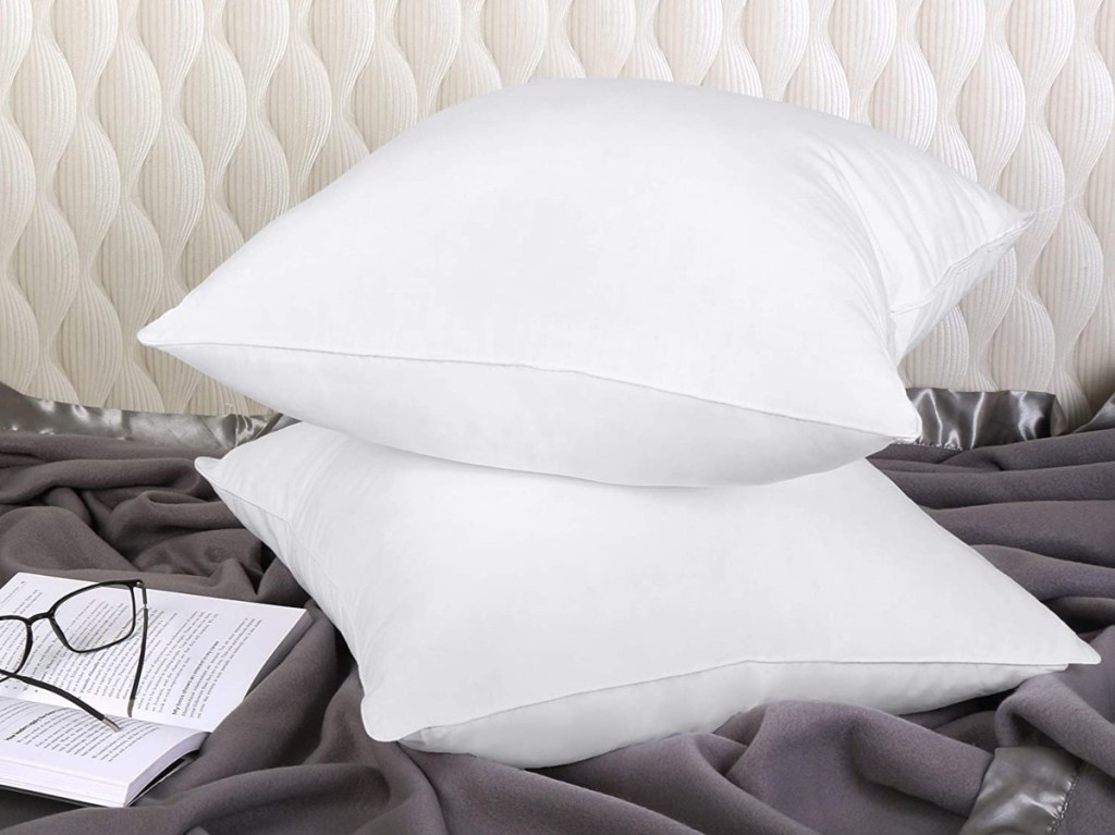 2 white pillows on bed with reading glasses and book