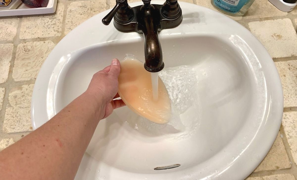 A hand washing a silicone sticky bra in the sink