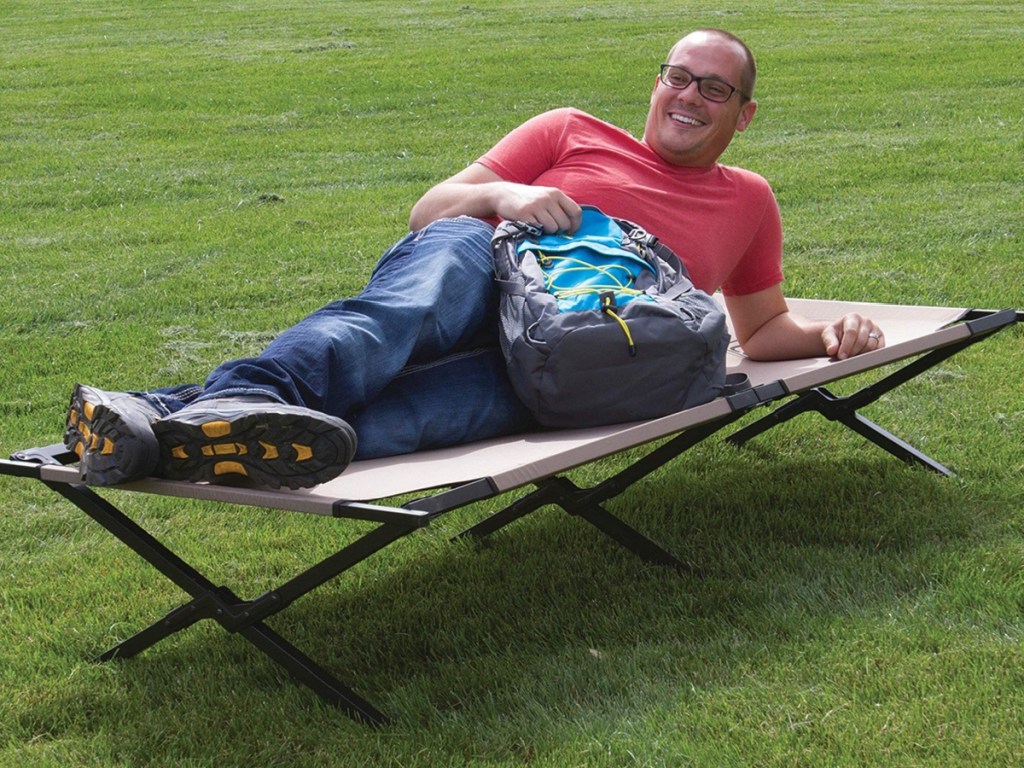 man laying on a folding cot next to a backpack