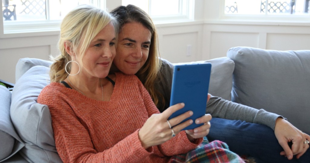 two women sitting on couch holding blue ereader