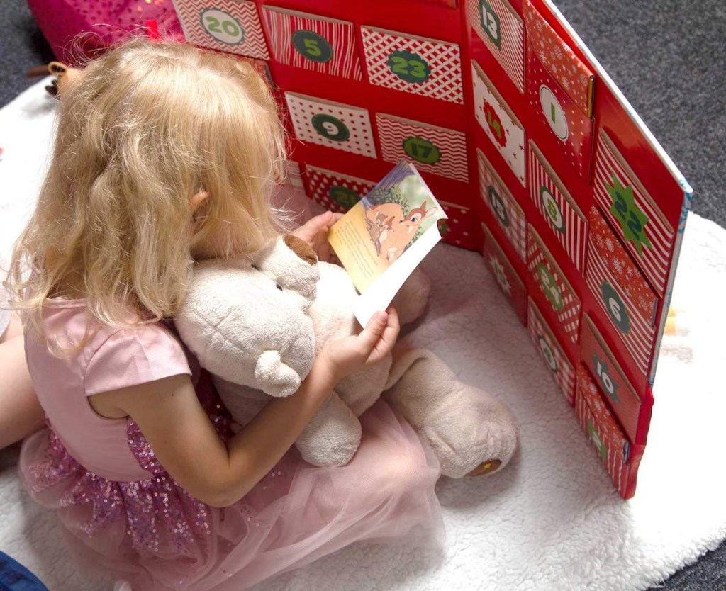 girl sitting on floor holding stuffed animal and disney book in front of large disney christmas story advent calendar