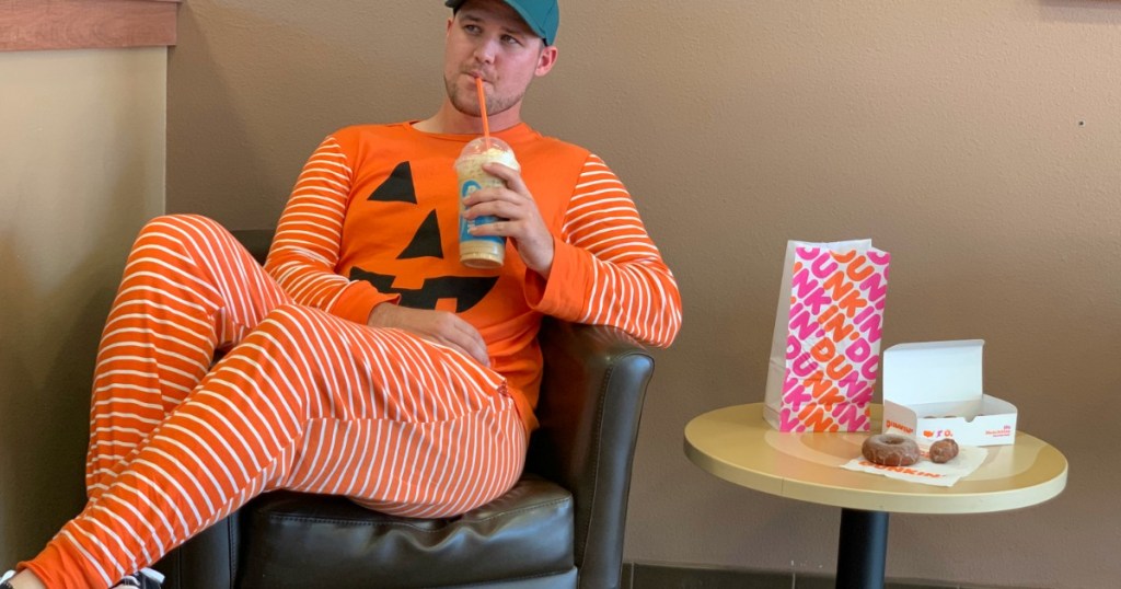 man wearing a pumpkin union suit drinking a dunkin pumpkin spice coffee