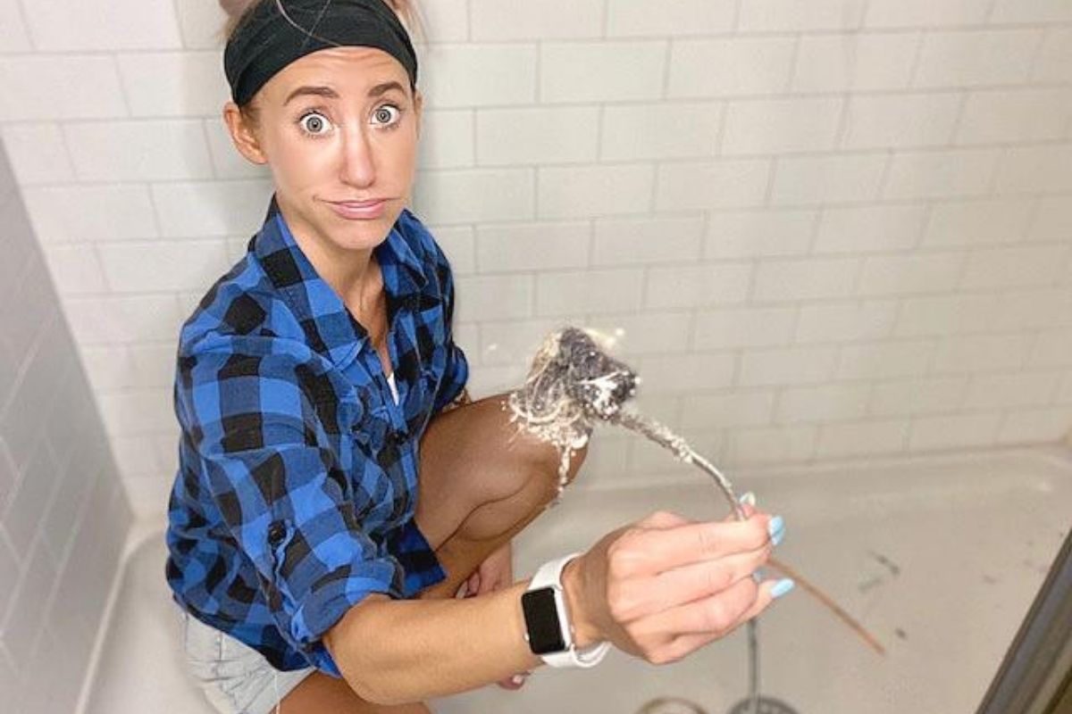 A woman holding a drain clog remover tool in the shower