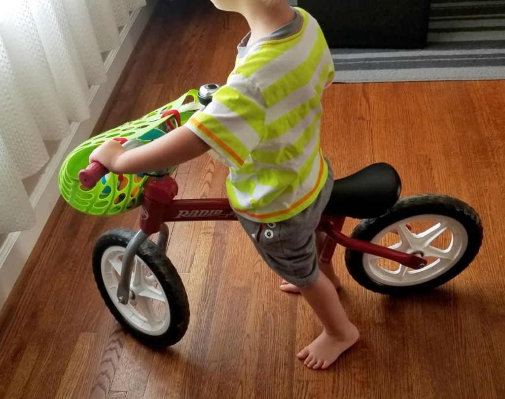 toddler boy on red bike with green basket attached to front