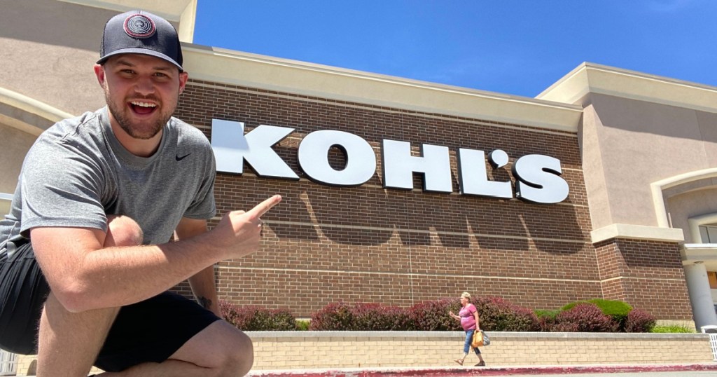 man kneeling in front of Kohl's store point to the sign