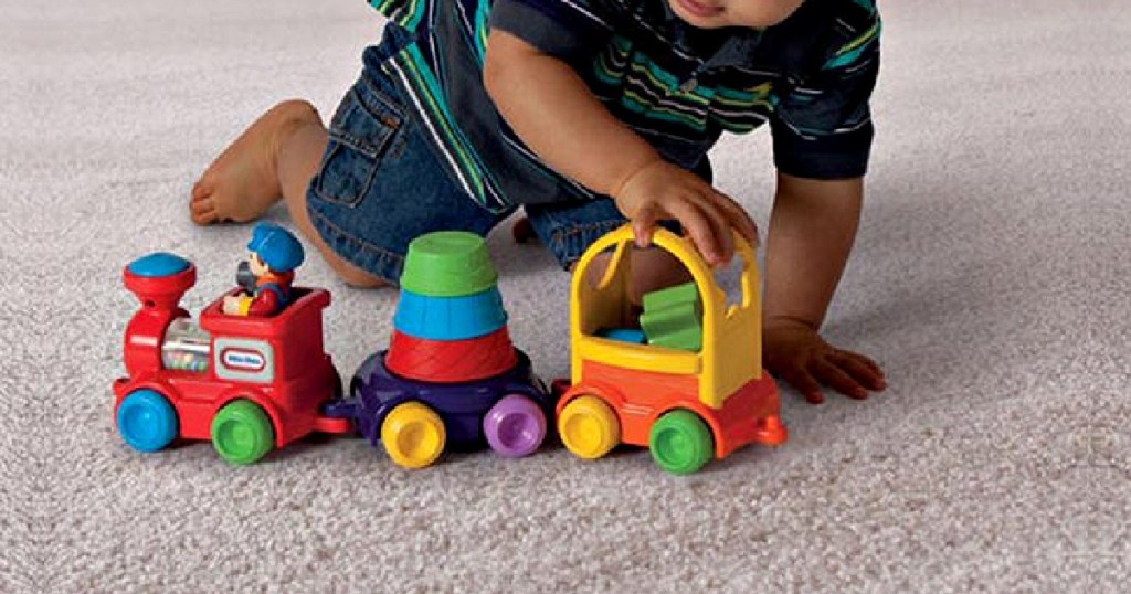 young boy playing with toy train and stack set on carpet