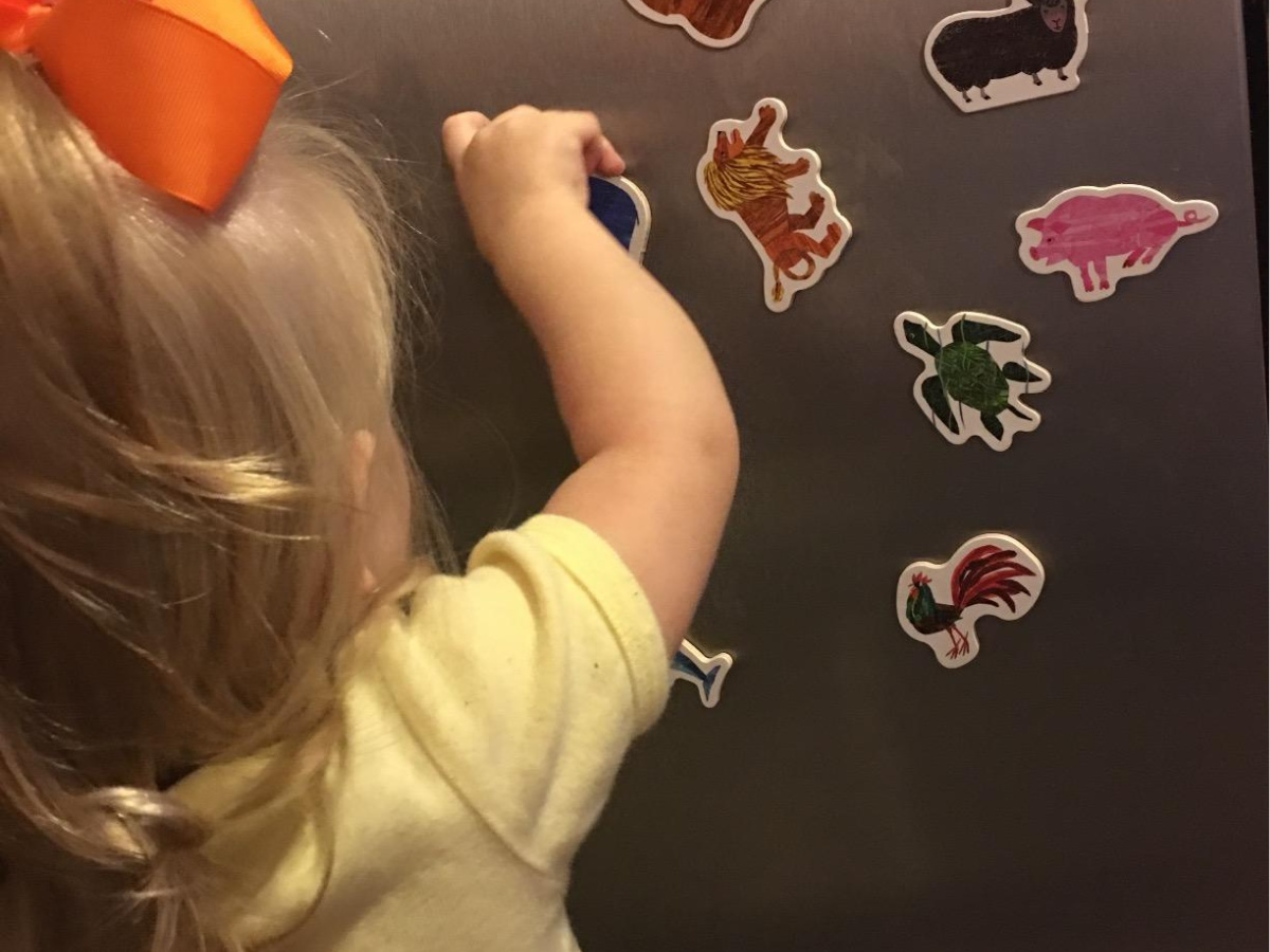 little girl putting magnets on stainless steel refrigerator