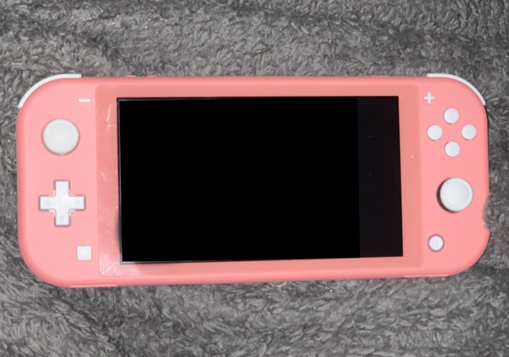 pink nintendo switch with white buttons laying on a grey fuzzy blanket