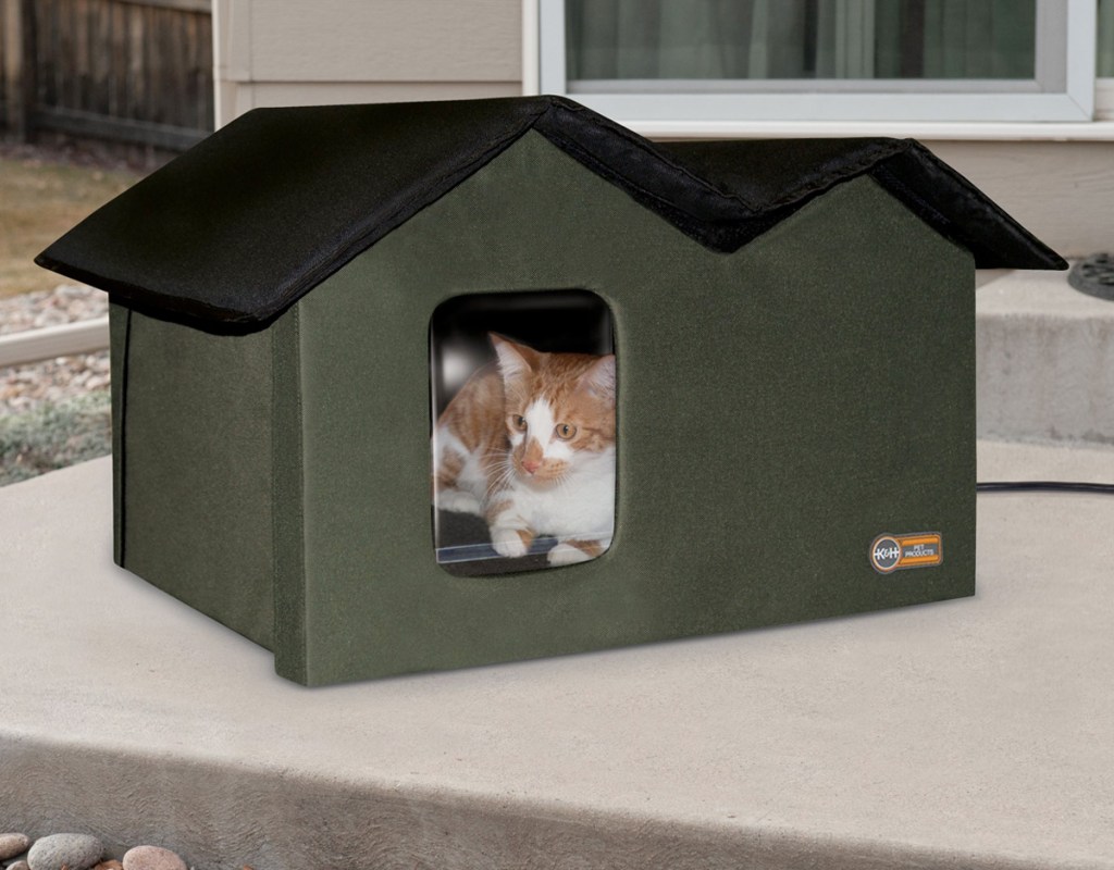olive green cat house with black roof on outdoor patio with orange and white cat inside