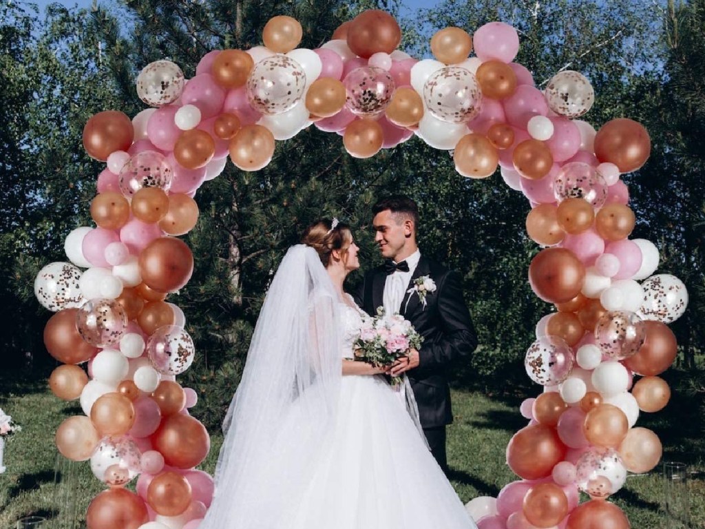 pink, gold, and white balloon arch over couple at outdoor wedding