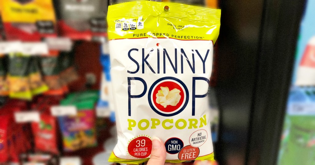 person holding up a small white and green bag of skinnypop popcorn