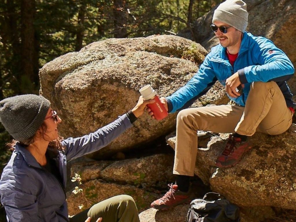 couple sharing reusable water bottle while sitting on rocks out in nature