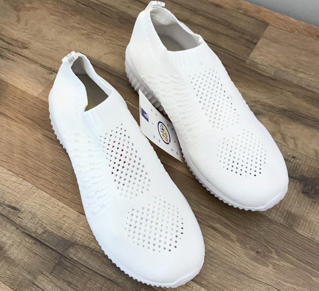 pair of white knit slip-on sneakers on hardwood floor