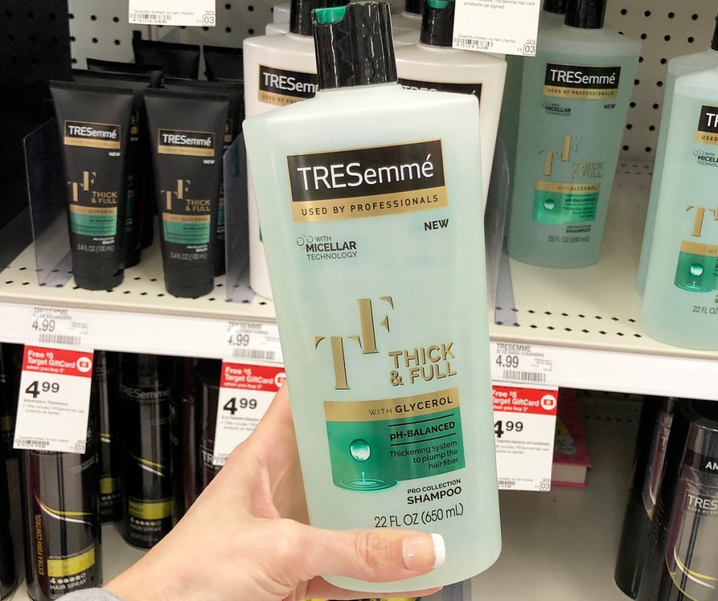 person holding up white and green bottle of Tresemme shampoo in front of Target shelf