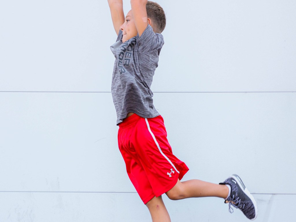 boy jumping wearing red pair of Under Armour Boys Maquina 2.0 Shorts