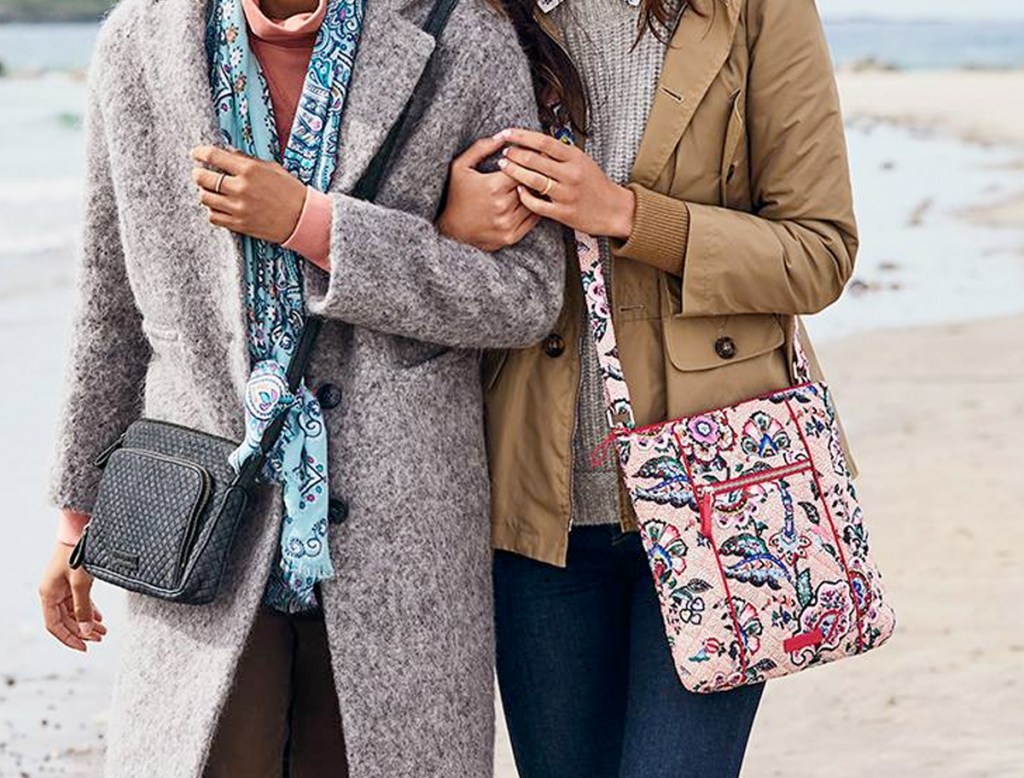 two women walking along beach with crossbody bags in grey and pink paisley print