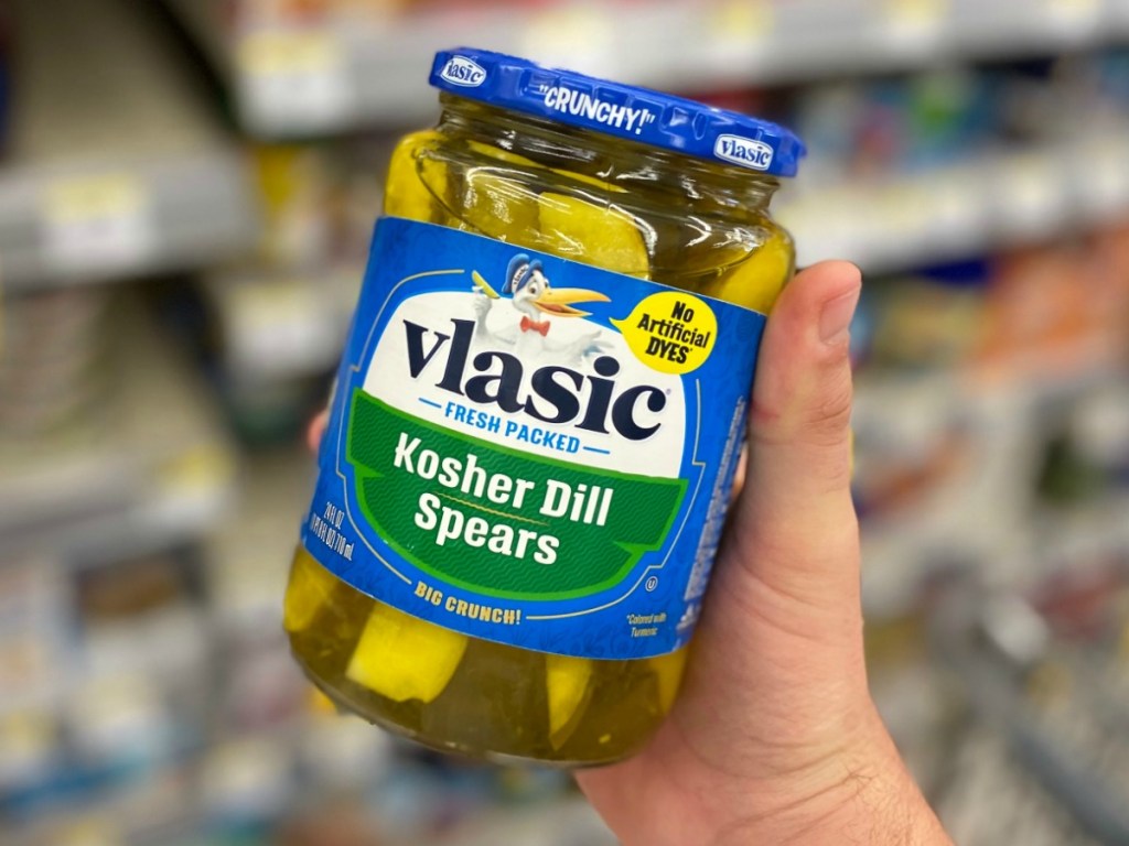 Man's hand holding a jar of kosher dill pickles near store shelf