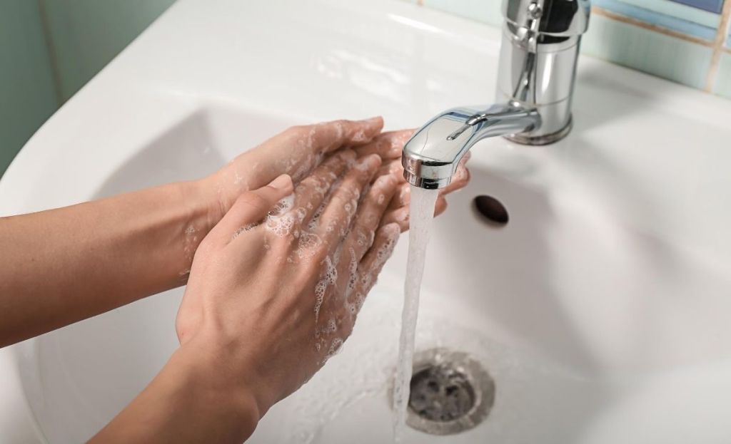a person washing hands with soap under a bathroom sink