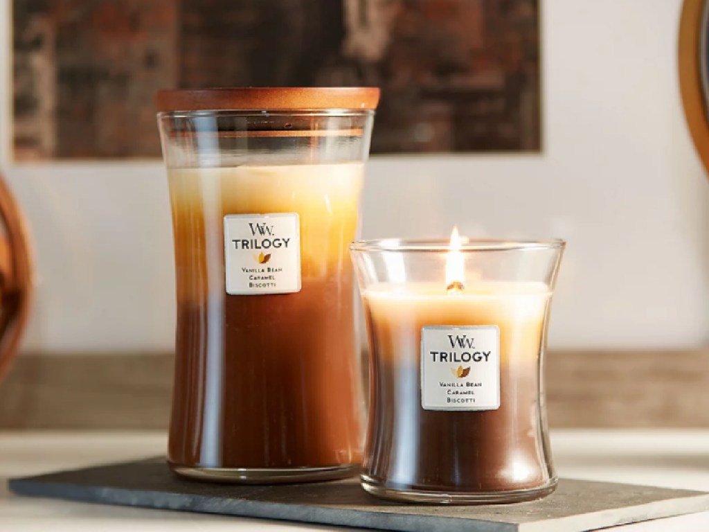 two WoodWick Trilogy Medium Hourglass Candles with one burning
