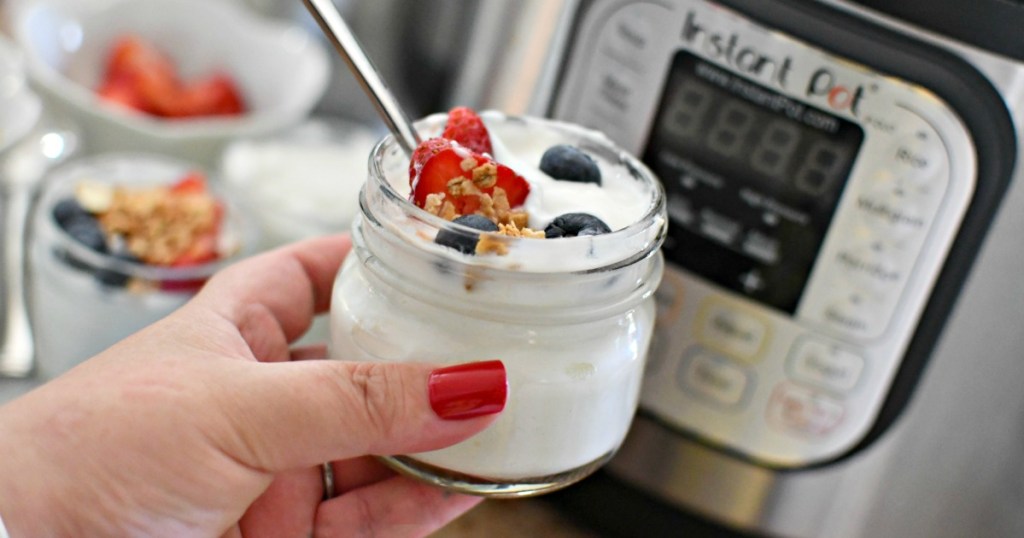 A hand holding a jar of yogurt from an instant pot