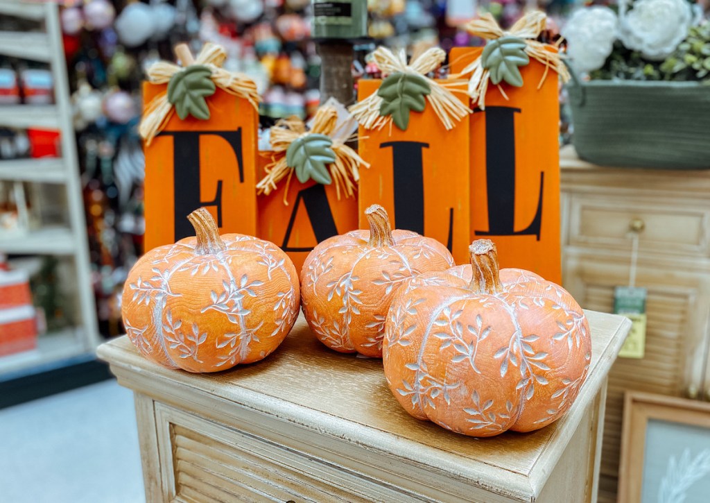 three orange pumpkins and fall sign on display in store