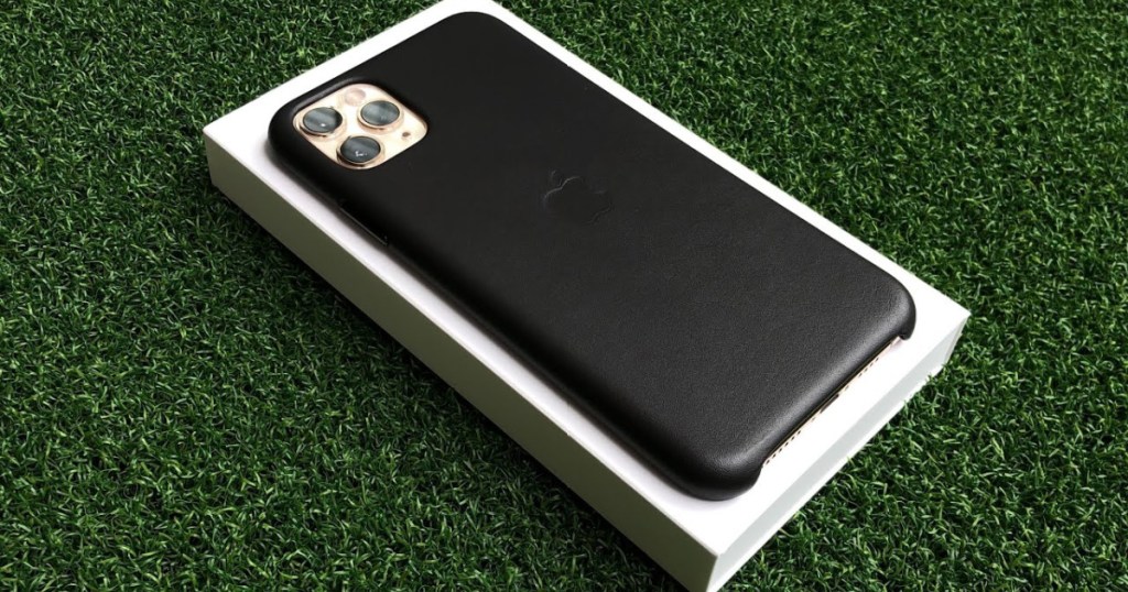 iPhone with black case sitting on white product box on green turf