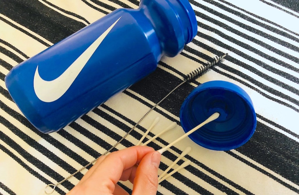 how to clean water bottles hand holding a qtip up to lid of blue nike reusable water bottle