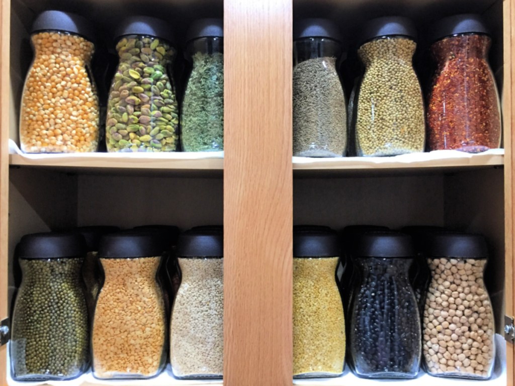 reused instant coffee jars with dried foods on shelves of cabinet