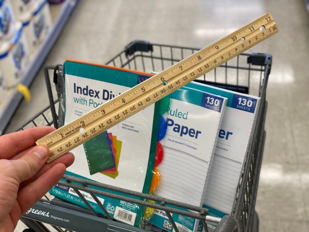 hand holder ruler in front of grocery cart with school supplies