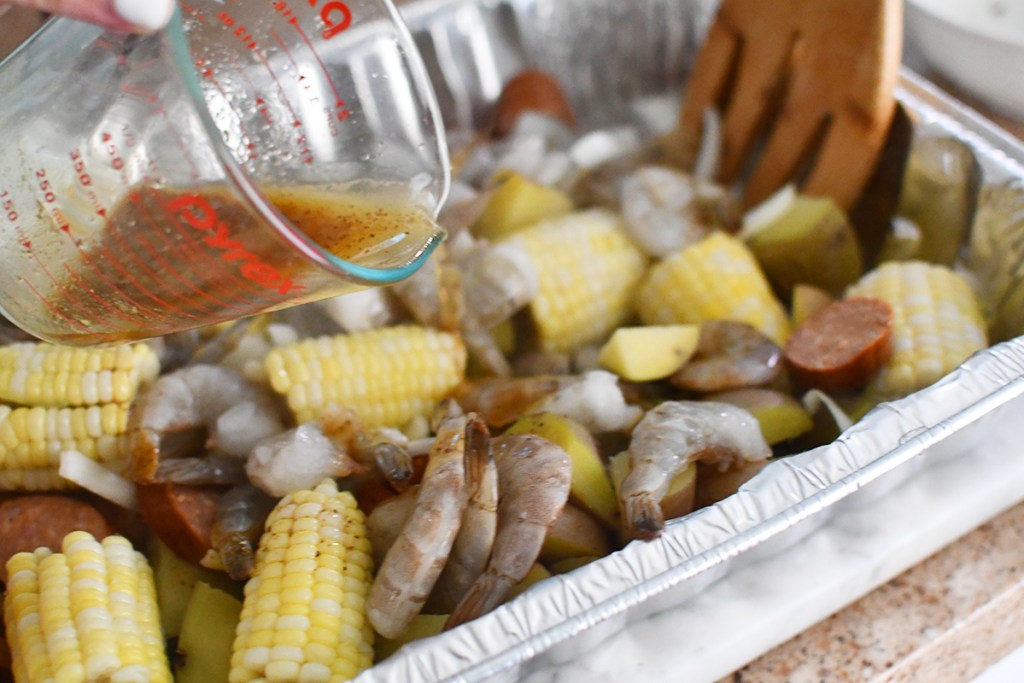 pouring butter and spices over shrimp, corn, potatoes, and sausage