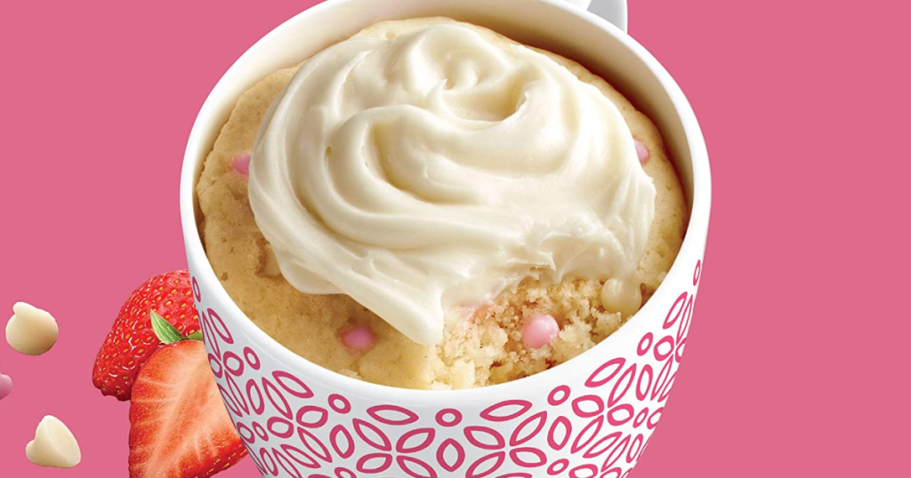 pink background with a mug that has a cake in it with icing and strawberries