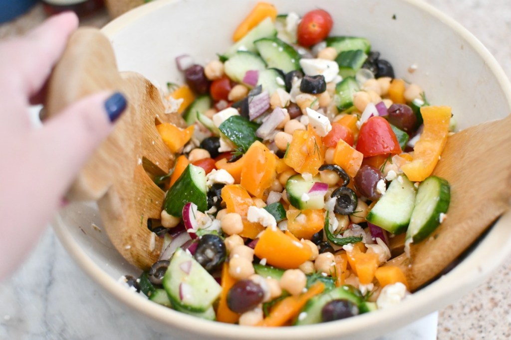 tossing greek chickpea salad in a bowl